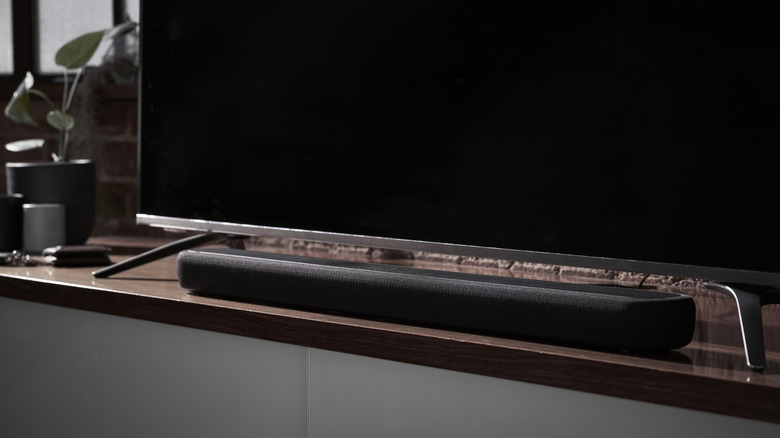A soundbar placed on a wooden surface right under a TV.