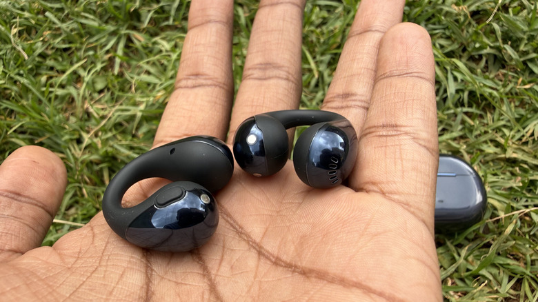 Person holding a pair of earbuds with case in the background