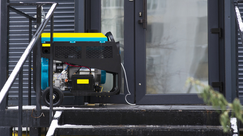 A small blue and yellow portable generator with wheels outside a home with a snowy porch