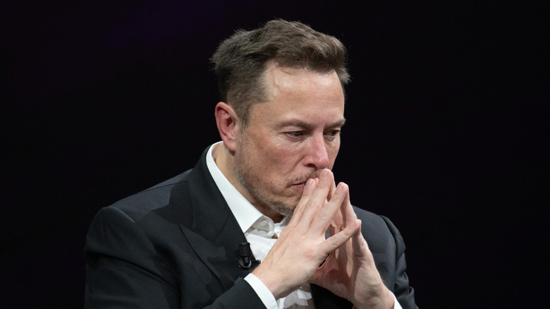 SpaceX CEO Elon Musk clasping his hands while in deep thought during a dialogue with the press.