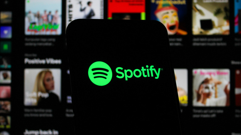 Phone showing Spotify logo with Spotify desktop app in background