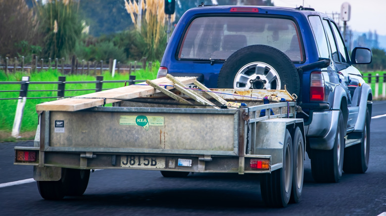 A blue SUV towing a dual-axle flatbed utility trailer