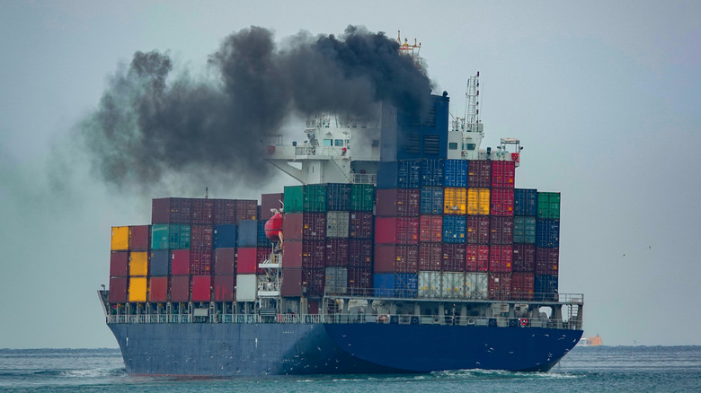 A large container ship, with containers piled on its deck, belching black smoke from its funnel.