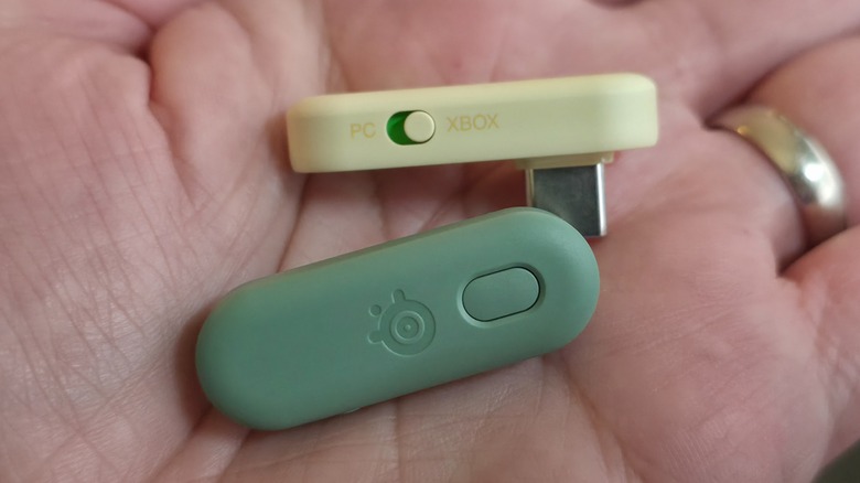 Two Arctis GameBud dongles in different colors held in a hand