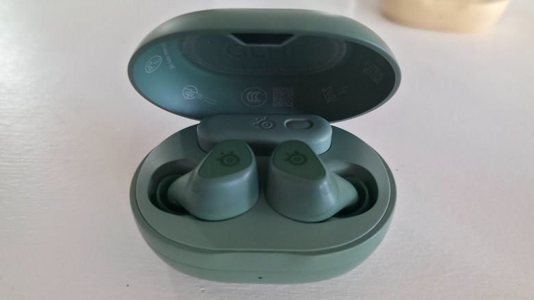A pair of Arctis GameBuds inside of its open case with the dongle