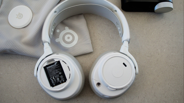 SteelSeries Arctis Nova Pro Omni gaming headset resting with accessories on a table with battery and USB-C ports exposed