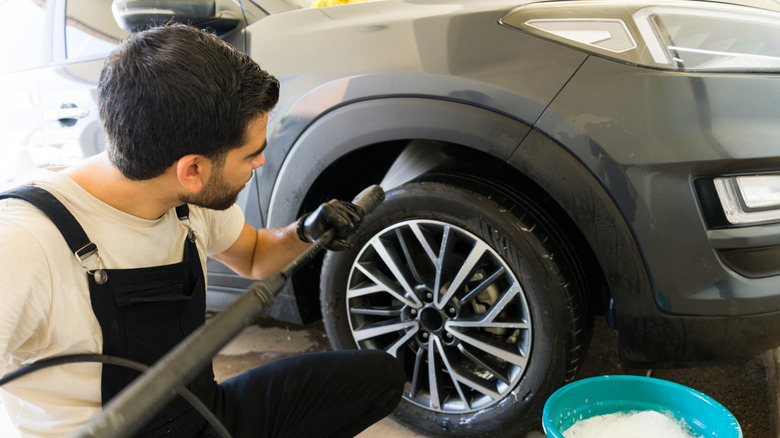 A man washes the undercarriage of a car, near the front wheels.