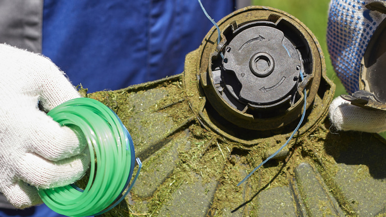 Close up of a gloved hand stringing a weed eater.