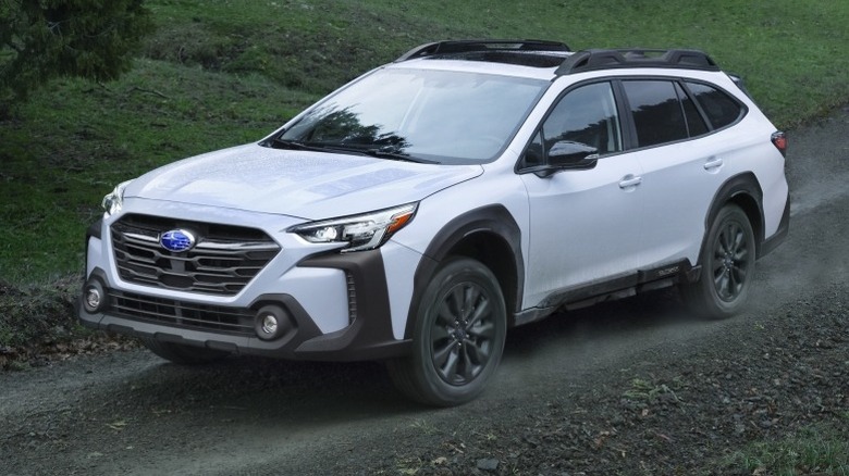 White Subaru Outback driving on a dirt road with lush green grass in the background