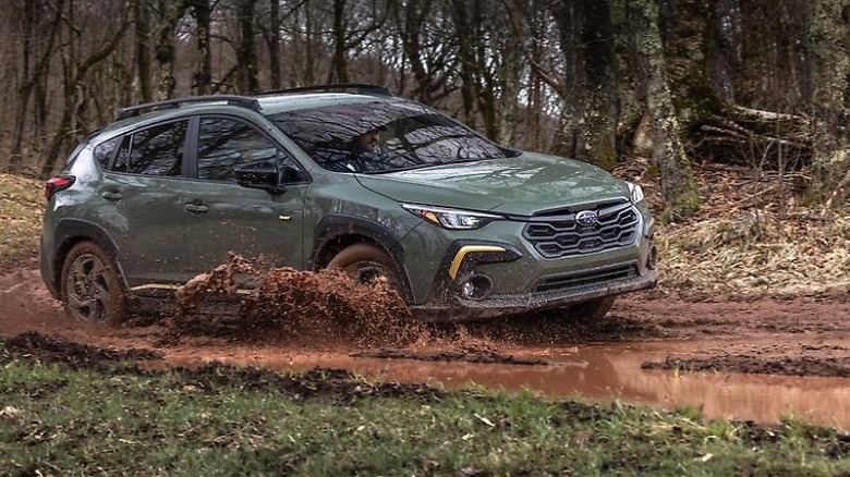 2025 Subaru Crosstrek Sport driving through a muddy off-road environment with trees in the background