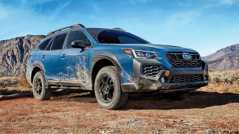 Geyser Blue Subaru Outback Wilderness parked on dirt surface with mountains in the background