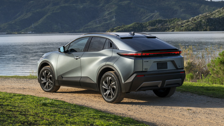 Rear 3/4 view of Toyota C-HR in gray, parked on dirt road in lakeside setting