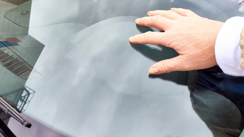 A hand on a windshield inspecting for damage.