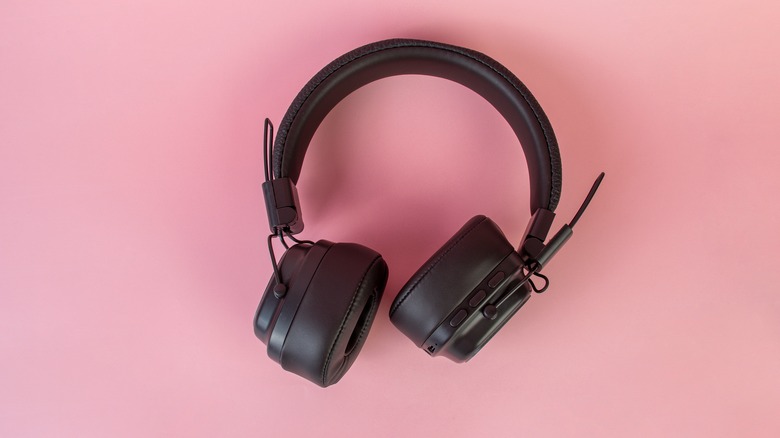 A set of black closed-cup wireless headphones on a pink background.