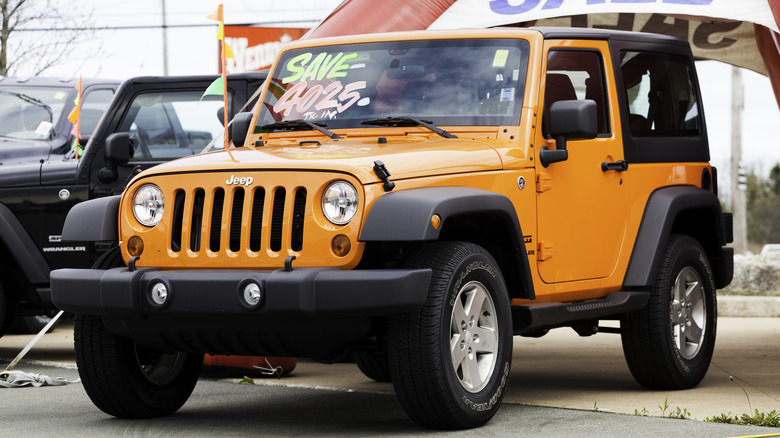 An orange Jeep Wrangler for sale on a car lot