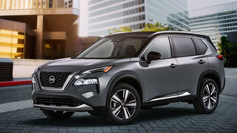 A silver 2021 Nissan Rogue parked in front of several modern office buildings