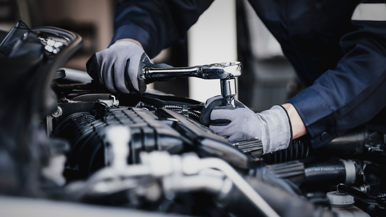 A mechanic wearing gloves working with tools on a car engine