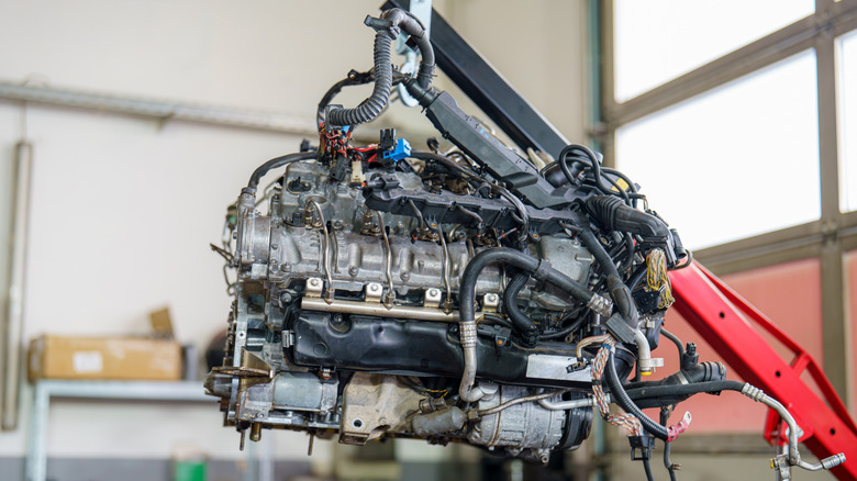 A mechanic is lifting an engine with a hoist inside a spacious automotive workshop