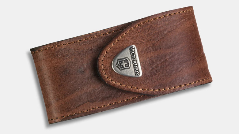 A brown leather pouch displayed sideways. It has brown stitching around the edge and a silver shield-like design that says Victorinox and has a Swiss Cross logo