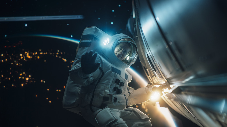 A Female Astronaut Posing in a Space Suit During a Spacewalk Mission on a Spaceship, Satellite or a Space Station. Adult Woman Looking at Camera, Smiling and Waving Hello Gesture with Hand