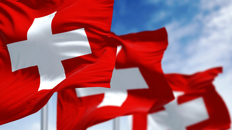 Three Swiss flags in a row against a blue sky