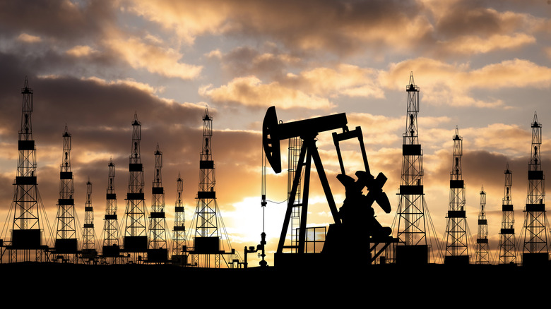 Oil field during sunset, with oil derrick and towers silhouetted against the background