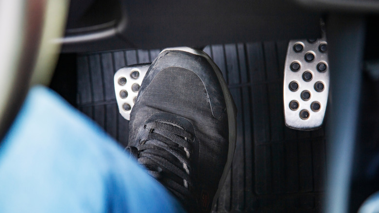 A black sneaker presses down on a car brake pedal.