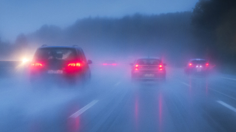 Car tail lights shine on the rear of four cars on a highway in the rain.
