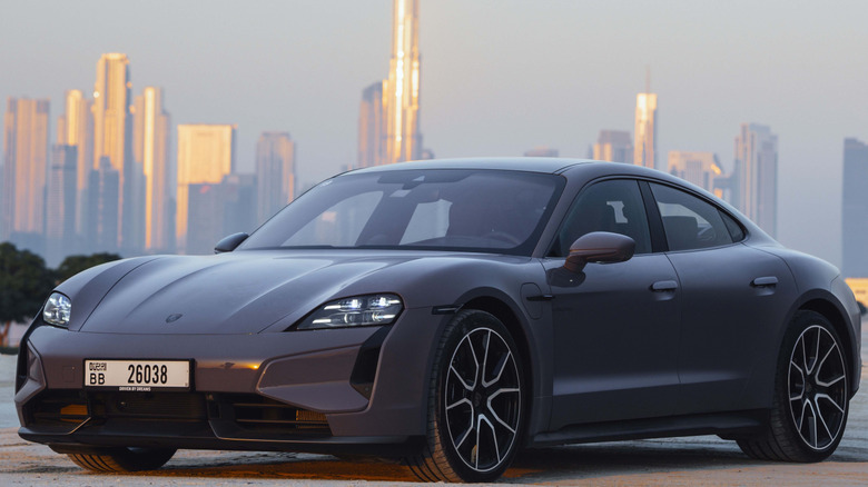 A black 2025 Porsche Taycan Turbo S overlooking the Dubai skyline, front-left three-quarter view.