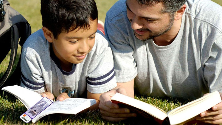 A father and son duo reading books while lying on grass