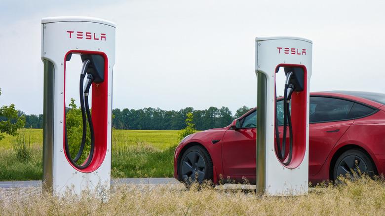 A red Tesla Model 3 charging at a rural Tesla Supercharger.