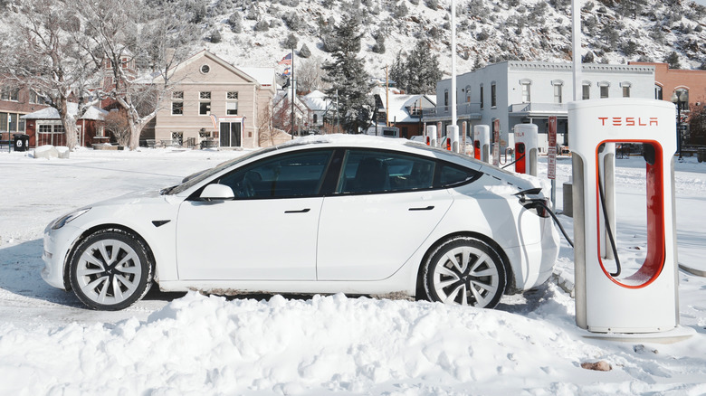 A white Tesla Model 3 charging at a snowy Supercharger.