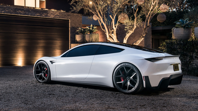 Rear 3/4 view of white Tesla Roadster parked in front of house.