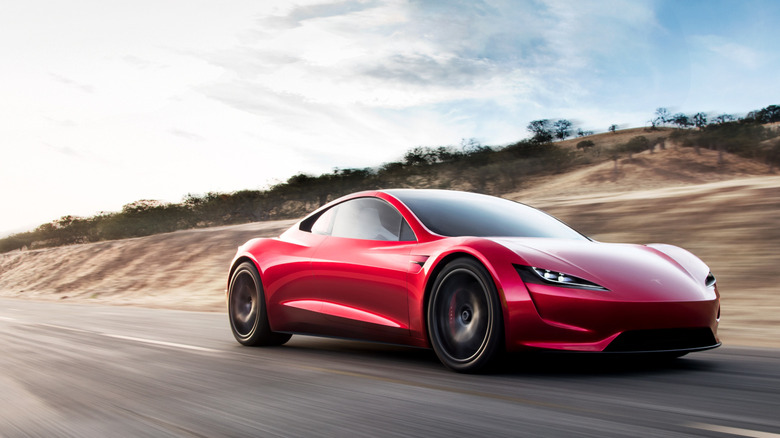 Front 3/4 view of red Tesla Roadster driving on highway.