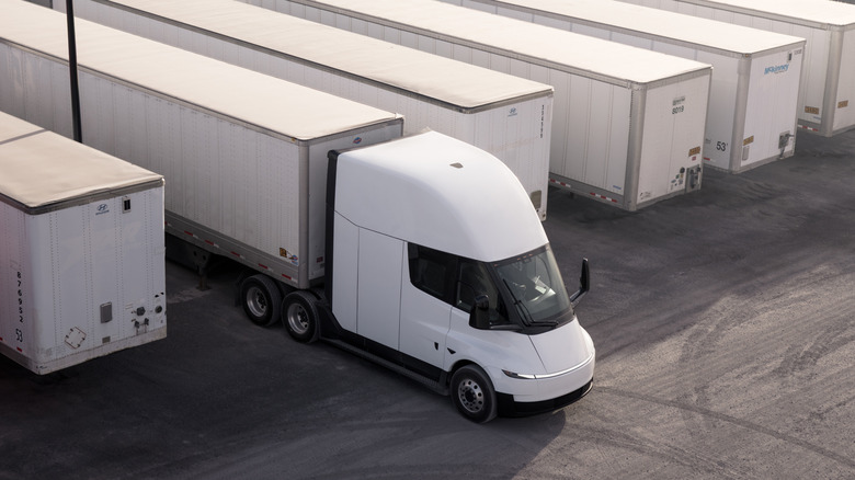 Overhead view of white Tesla Semi pulling trailer at freight depot.