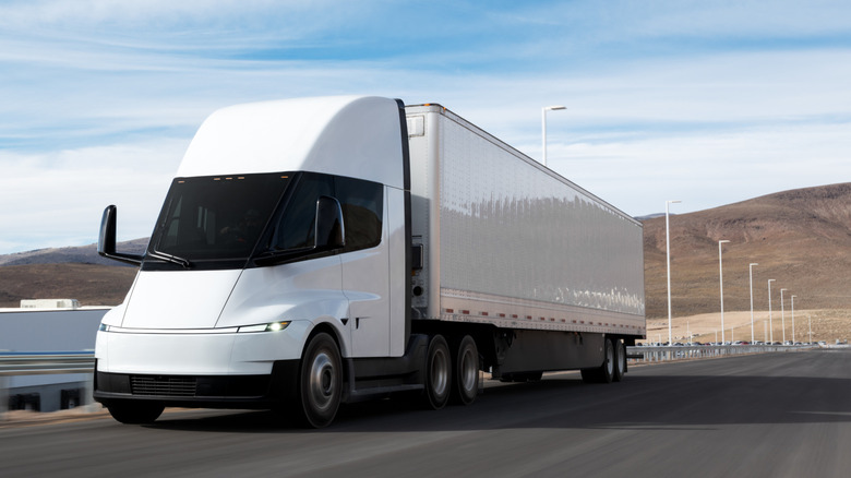 Front 3/4 view of white Tesla Semi towing white trailer in desert.