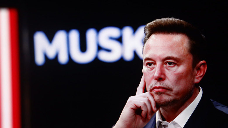 Elon Musk in foreground with "Musk" in lights behind him