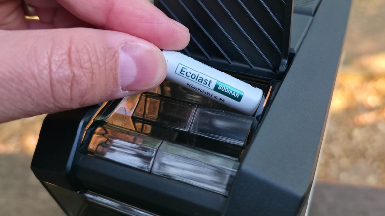 Two fingers holding a AAA rechargeable battery being placed into the Ostation 2 Pro.