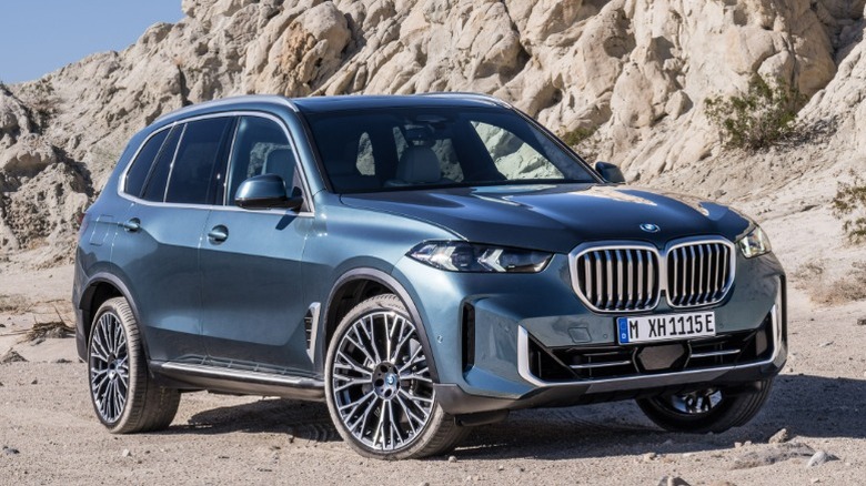 Teal BMW X5 parked on sand with rocks in the background