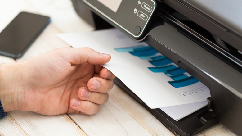 Person pulling a printed image from a printer tray.