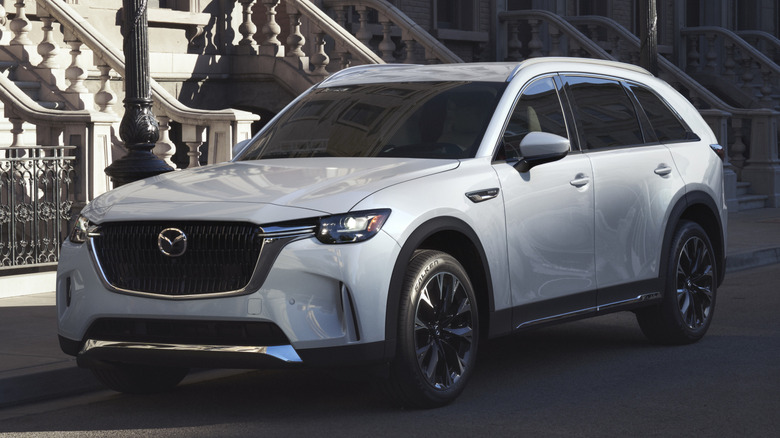 White Mazda CX-90 PHEV parked near a sidewalk in front of apartments