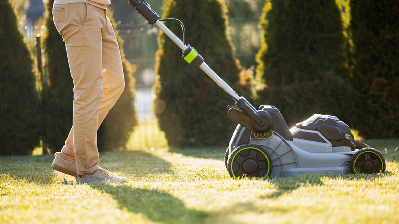 Landscaper mowing a lawn with a gray and green mower