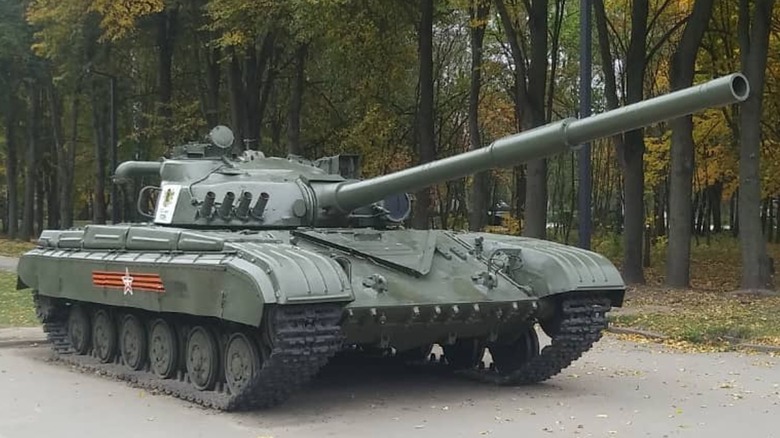 A parked T-64 Main Battle Tank sitting in front of a thicket of trees