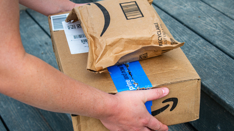 A person picking up Amazon packages from wood deck