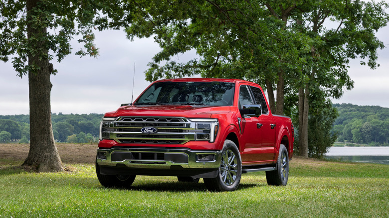 A 2027 red Ford F-150 Lariat parked on grass in front of several trees