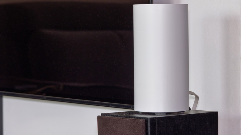 A mesh wi-fi node on a small wooden cabinet next to a TV