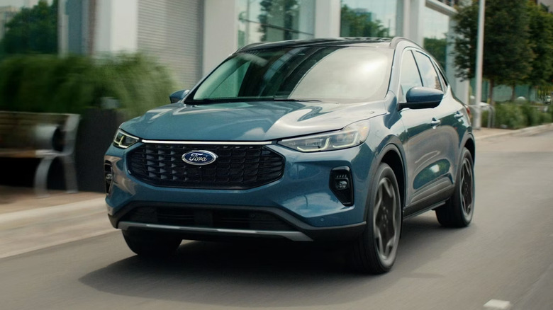 A light metallic blue 2026 Ford Escape SUV moving down a city road, with the background motion blurred.