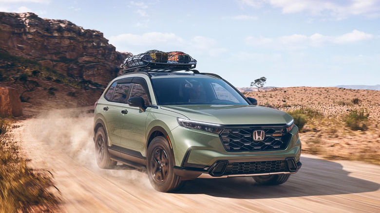 A green 2026 Honda CR-V SUV moving down a dusty cliffside road at speed, kicking up mud behind it.
