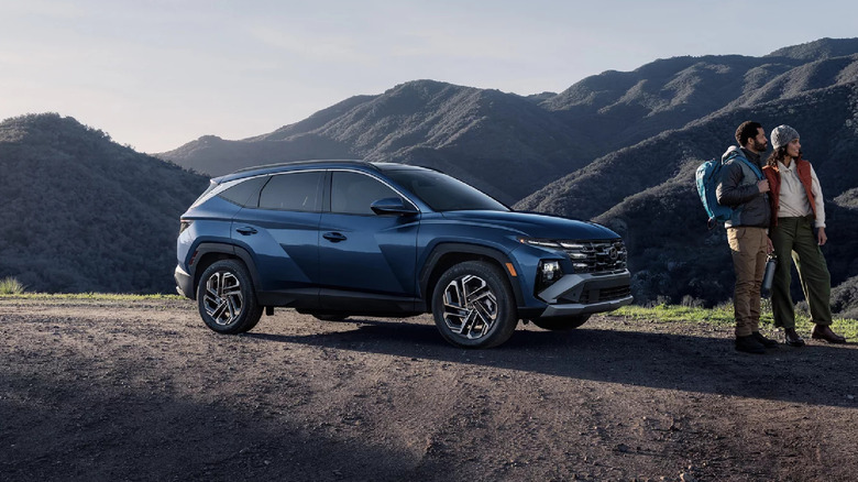 A dark blue 2026 Hyundai Tucson SUV standing on an unpaved section of land with mountains in the back.