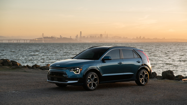 A 2025 Kia Niro PHEV version standing on a paved section of road near a body of water in the evening at dusk time.